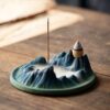 A beautiful ceramic Backflow Incense Burner Mountain Style, with a mesmerizing smoke waterfall flowing into its basin and an incense stick burning.