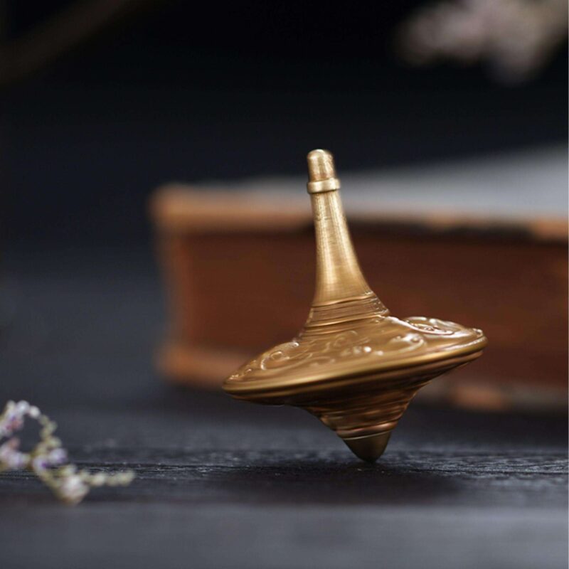 An artisanal Celestial Dragon brass fidget spinner resting on a dark wooden surface, showing its intricate traditional carvings.
