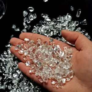 A hand holding a handful of sparkling, clear quartz demagnetizing stone chips against a black background to show their quality.
