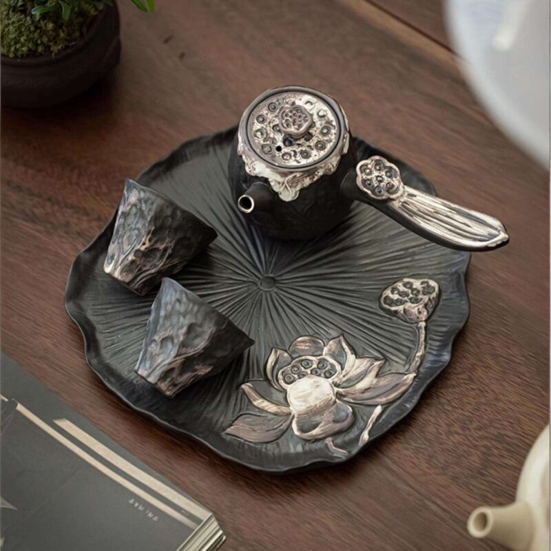 A close-up detail shot of the ornate, silver-accented lid of a handmade ceramic teapot, showing its fine craftsmanship.