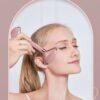 A woman demonstrates how to use a jade gua sha facial roller on her face.