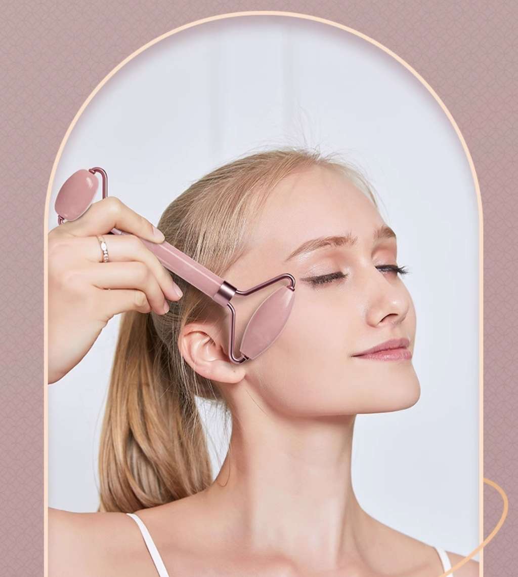 A woman demonstrates how to use a jade gua sha facial roller on her face.