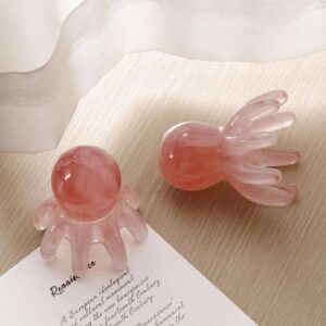 A beautiful pink marbled resin octopus scalp massage comb held gently in the palm of a hand.