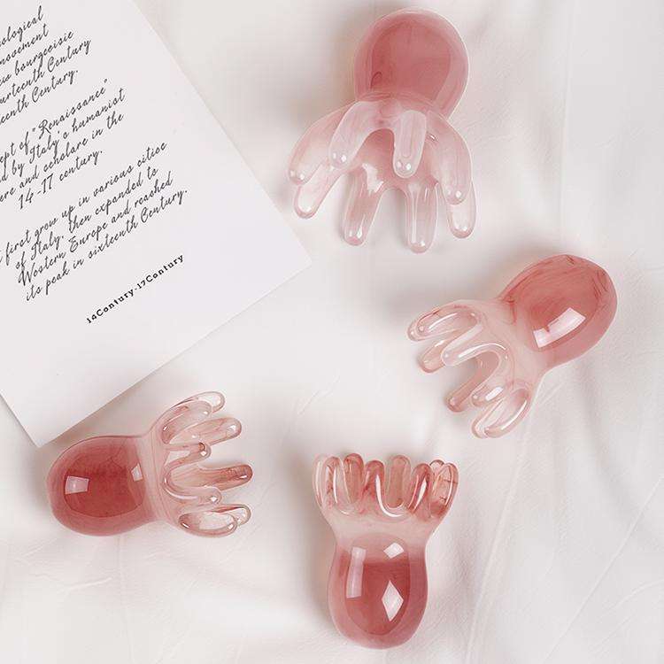 A beautiful pink marbled resin octopushead massage tool held gently in the palm of a hand.