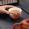 A person enjoying a Gongfu tea ceremony, pouring tea into an exquisite enameled handmade ceramic teacup.