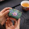 A person enjoying a Gongfu tea ceremony, pouring tea into an exquisite enameled handmade ceramic teacup.
