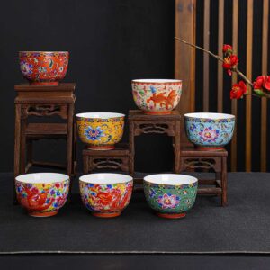 A pair of hands holding four ornate, Enameled Handmade Ceramic Teacup in vibrant red, green, blue, and yellow with interlocking lotus designs