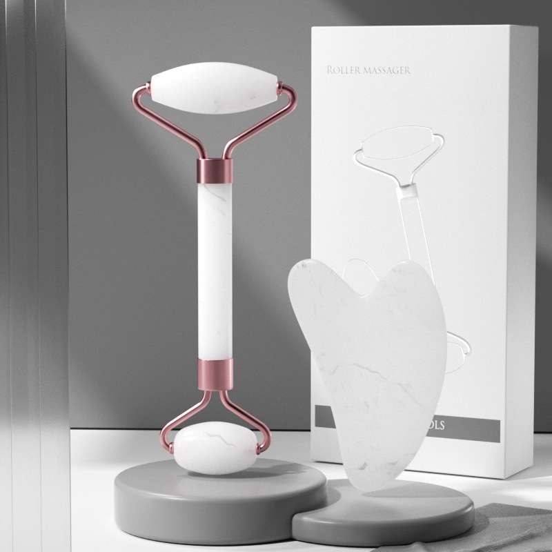 A minimalist white jade facial set containing both a gua sha sculpting tool and a massage roller on a neutral background.