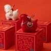 Close up of a red year of the horse ceramic ornament showing the golden coin detail, greeting scroll, and glossy porcelain finish for Lunar New Year decoration.