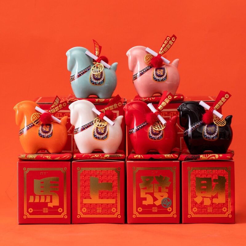 Close up of a red year of the horse ceramic ornament showing the golden coin detail, greeting scroll, and glossy porcelain finish for Lunar New Year decoration.