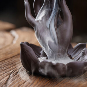 Zen style Buddha hand backflow incense burner placed on a wooden tea table with stick incense burning, creating a meditative atmosphere.
